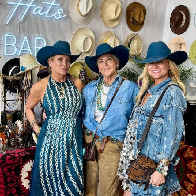 Three women in blue cowboy hats at the Topped Hats booth beneath a white Hats Bar LED neon sign