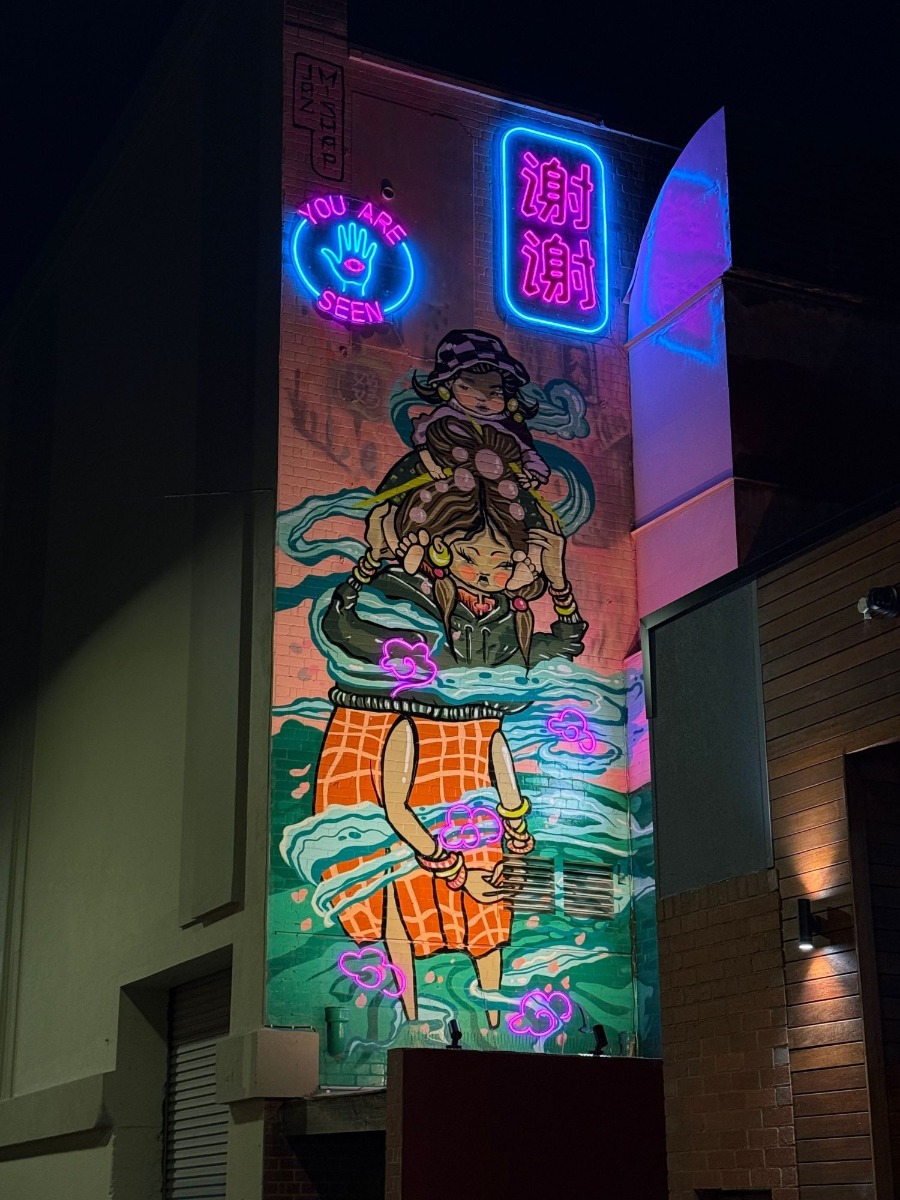 Urban art mural by @jazmishap on the side of a building with Custom Neon® signs as creative lighting elements