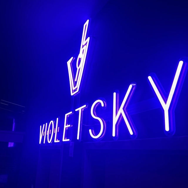 Blue custom neon 'Violetsky' sign with a lightning bolt icon glowing in a dark room
